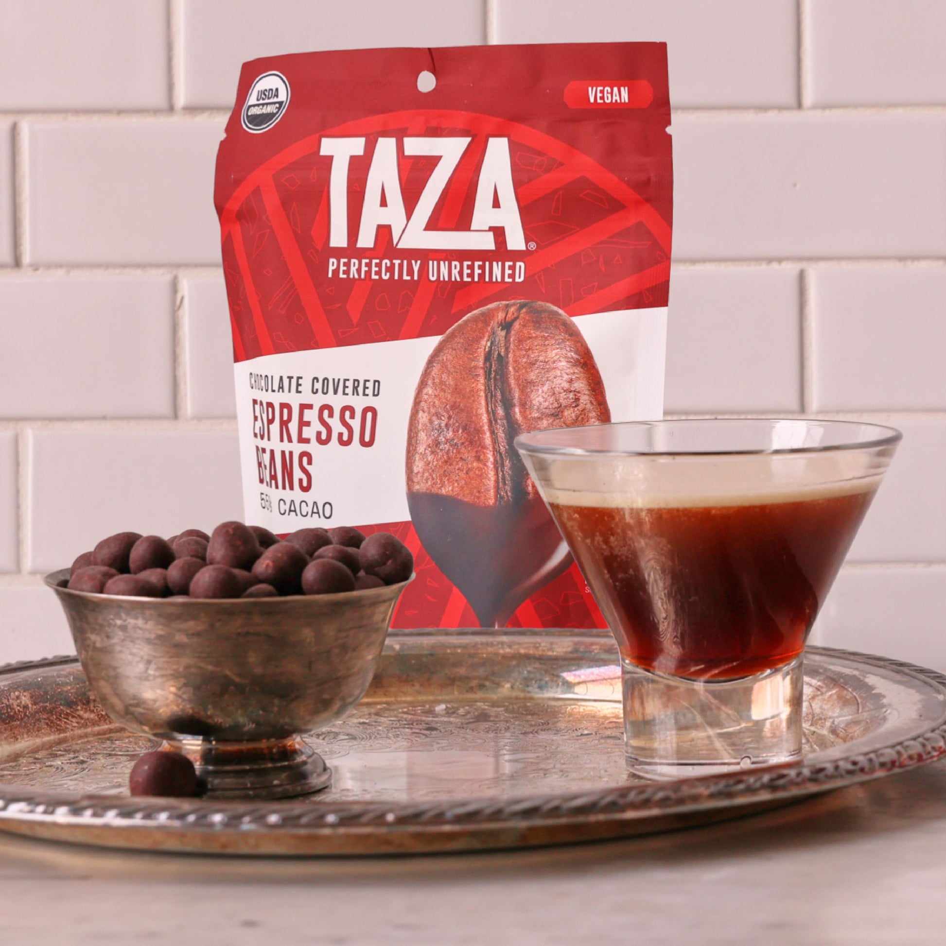 Bag of Chocolate Covered Espresso Beans in a kitchen setting near open chocolate covered espresso beans and an espresso beverage.