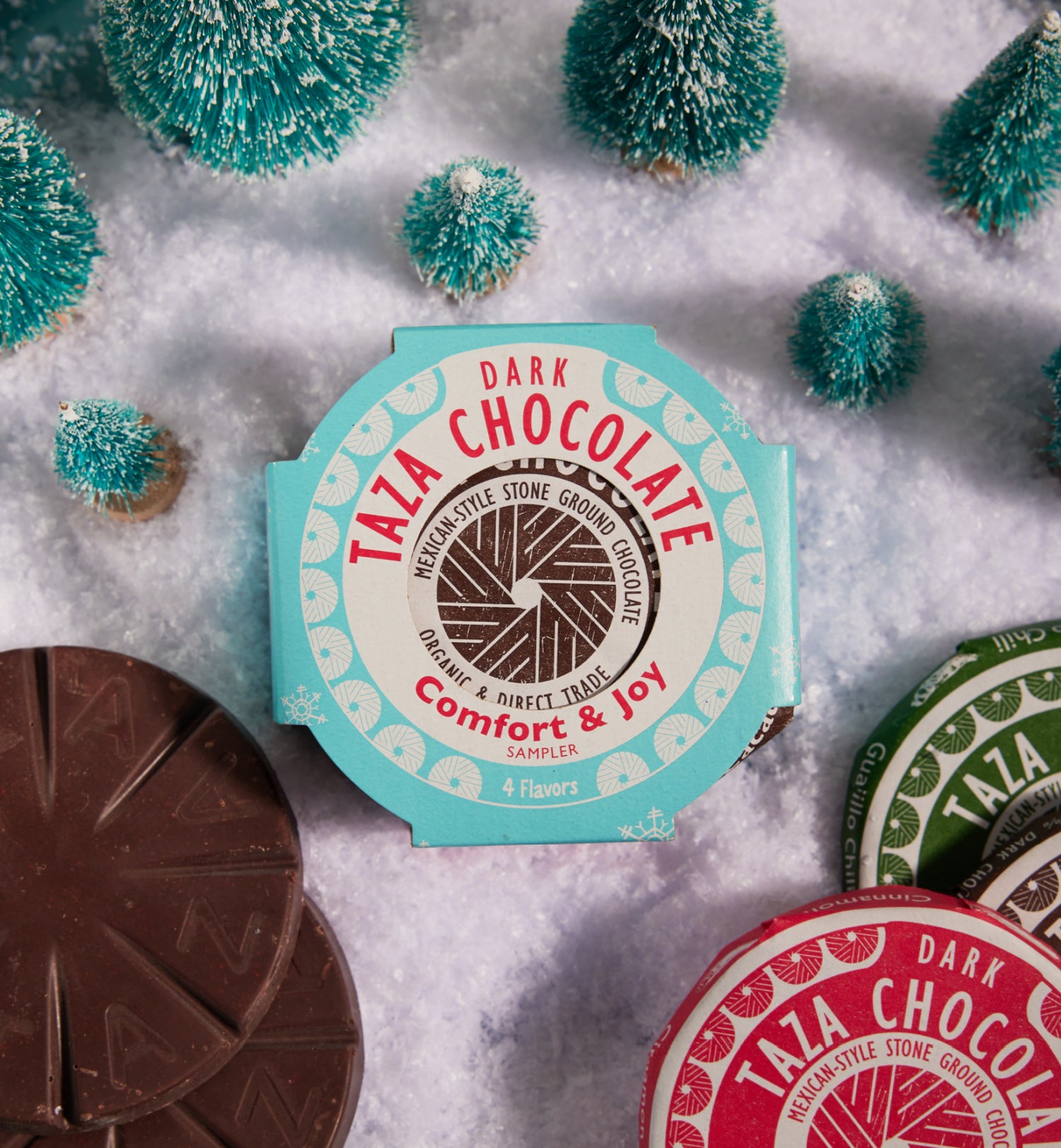 Taza Chocolate Comfort & Joy Sampler packaging with chocolate pieces on a snowy background