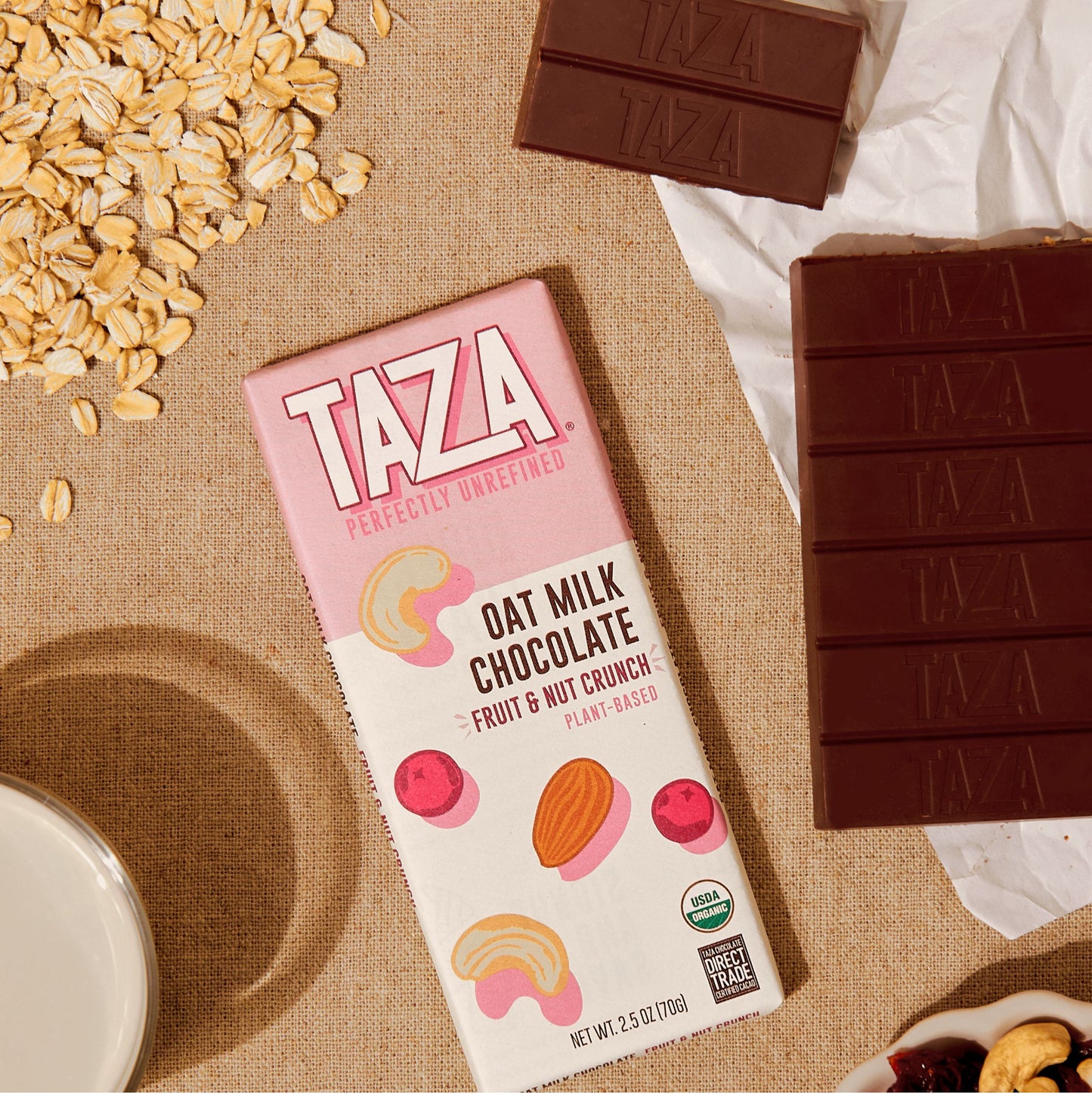 Fruit & Nut Crunch Oat Milk Bar laying next to unwrapped chocolate and oats.
