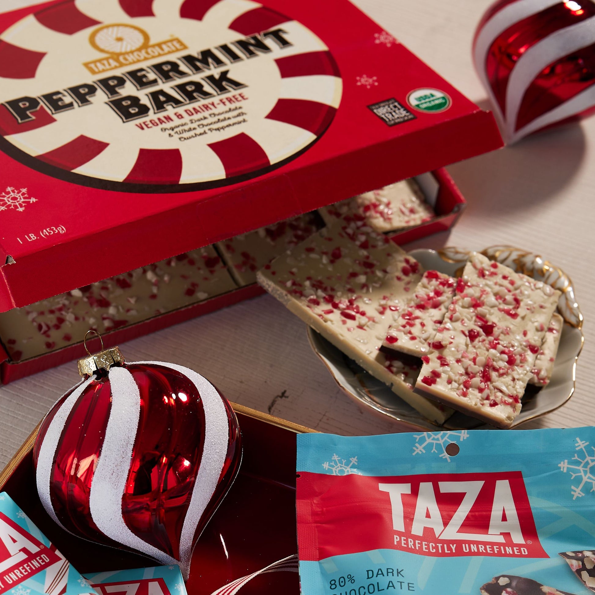 Box of open Peppermint Bark amongst holiday products and ornaments.