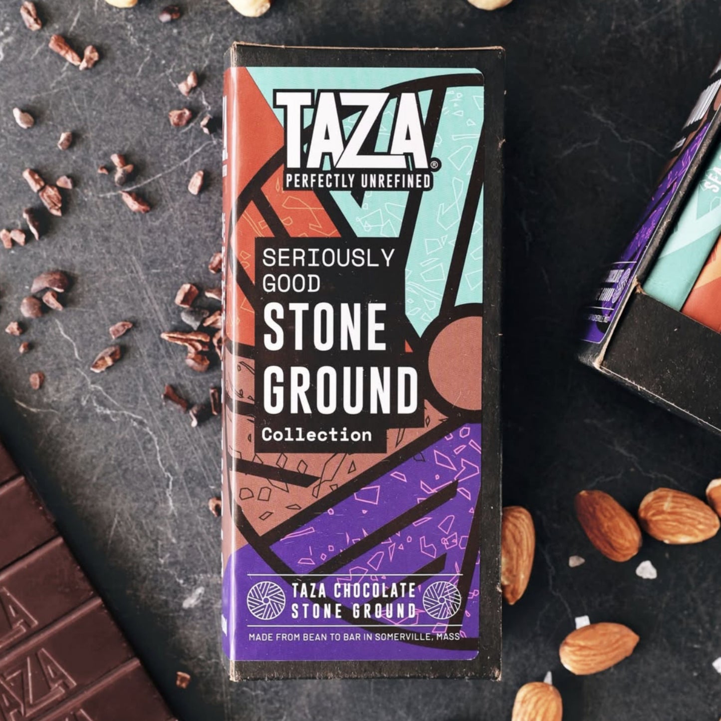 Seriously Good Stone Ground Collection box on a dark stone background surrounded by salt, almonds, and unwrapped chocolate.