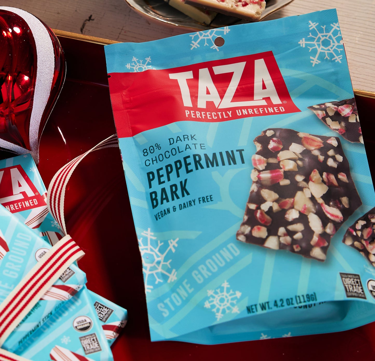 Taza peppermint bark packaging on a red surface with holiday decorations.