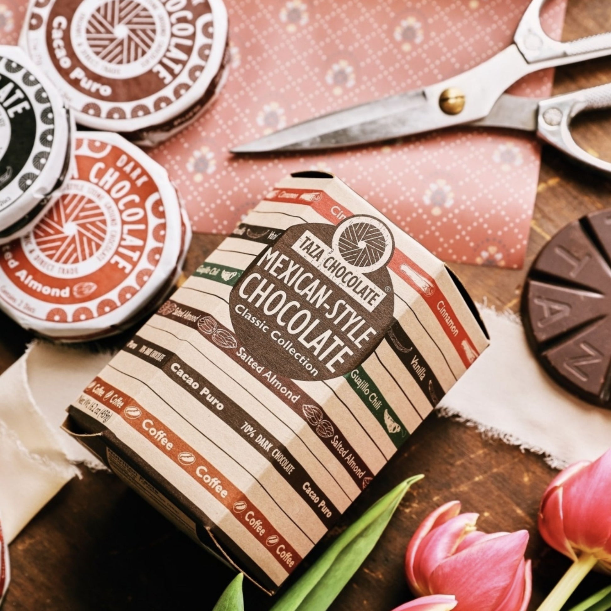 Closeup of the Mexican-Style Chocolate Classic Collection box surrounded by wrapped and unwrapped discs, and gift wrapping supplies.