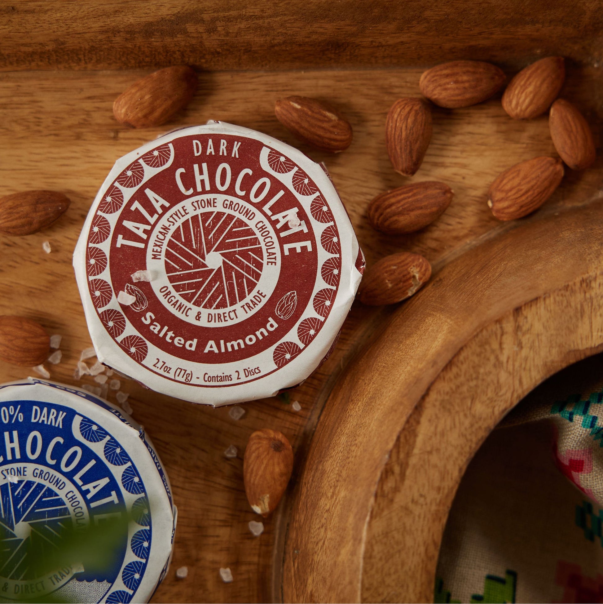 Close up of Salted Almond Chocolate Disc surrounded by salt and almonds.