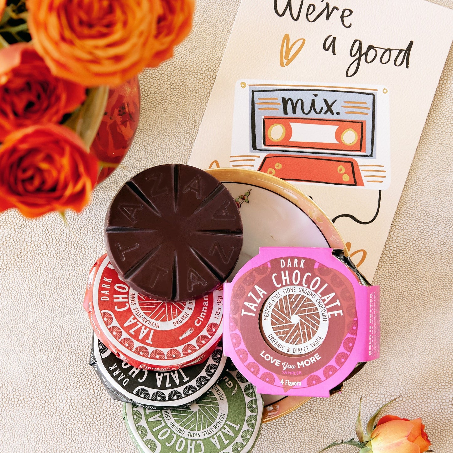 Taza chocolate Valentine's day disc sampler with colorful packaging on a textured surface with flowers.