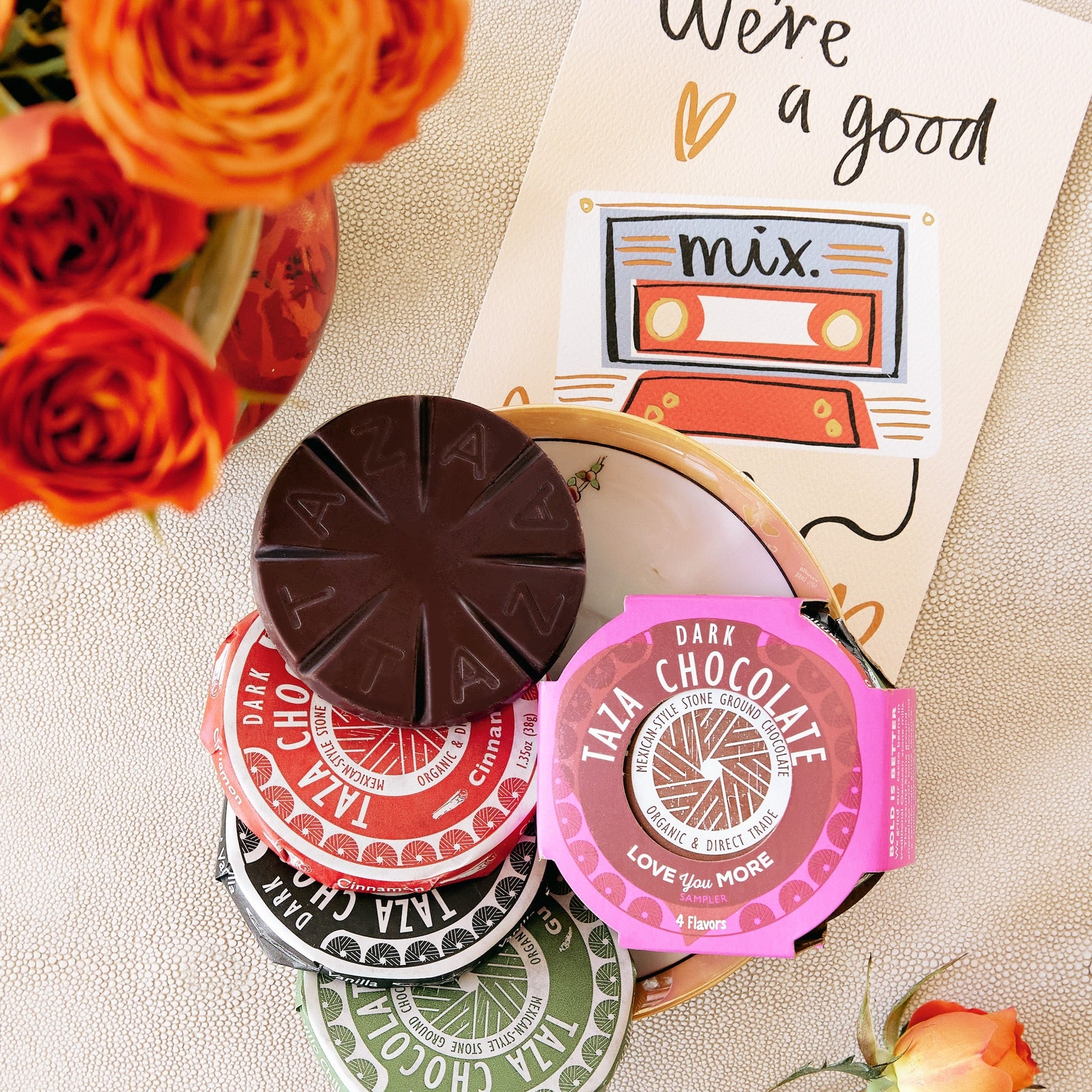 Taza chocolate Valentine's day disc sampler with colorful packaging on a textured surface with flowers.