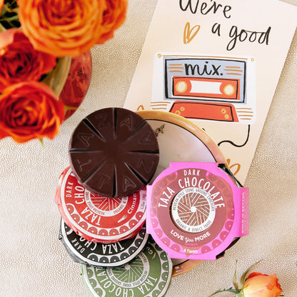 Taza chocolate Valentine's day disc sampler with colorful packaging on a textured surface with flowers.