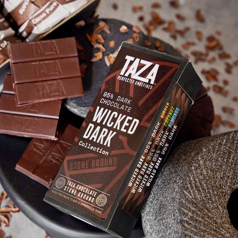 Wicked Dark Collection box next to unwrapped chocolate in a dark stone setting.